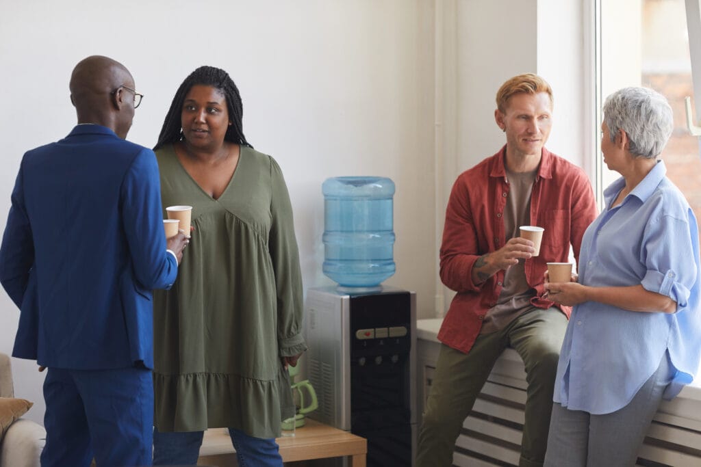 group of people drinking coffee and chatting while standing by water cooler