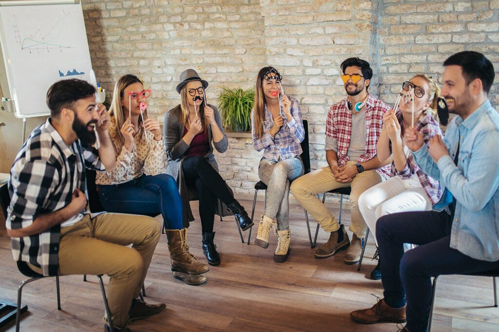 Group of co-workers sitting in a circle with funny and silly props placed in front of their faces