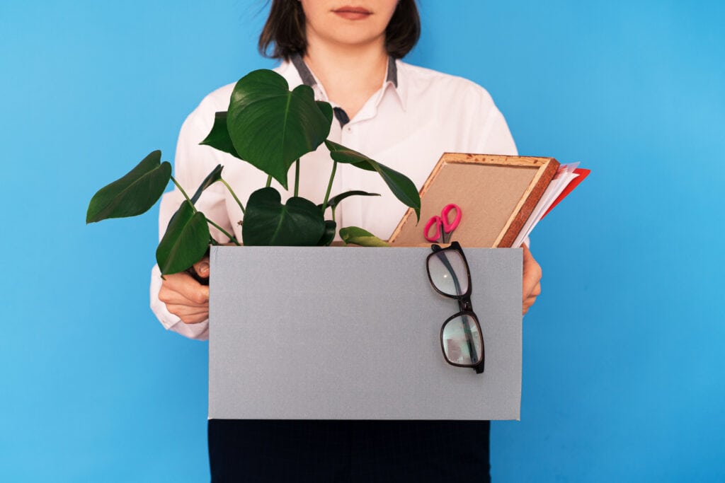 Girl in a white shirt holding a box of office supplies.