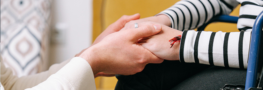 Person holding the hand of a person in a wheelchair